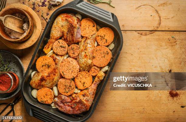 chicken legs baked with garlic and sweet potatoes in a cast iron baking dish on a wooden table with spices - sweet potato stock pictures, royalty-free photos & images