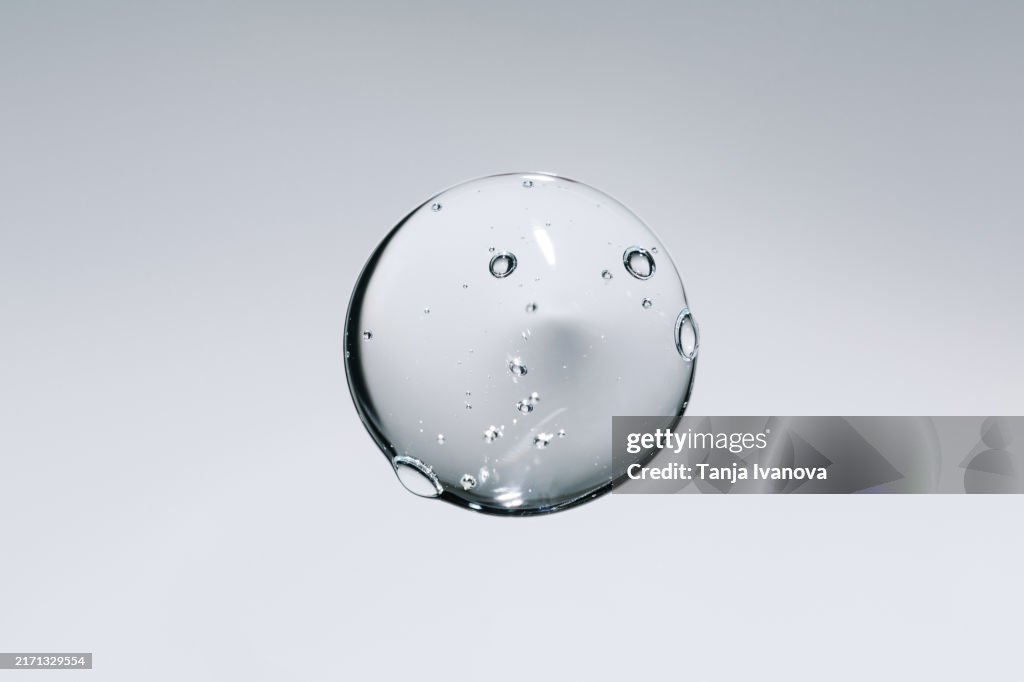Liquid drop of gel. Serum transparent cosmetic sample texture with bubbles on gray background