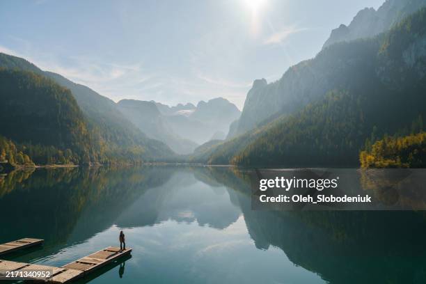 donna sul molo vicino al lago e guardando la vista di gosausee e delle montagne - ambientazione tranquilla foto e immagini stock