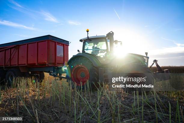 silhouette des traktors, der einen anhänger auf einem bestellten feld mit sonnenhintergrund zieht - landwirtschaftliche tätigkeit stock-fotos und bilder