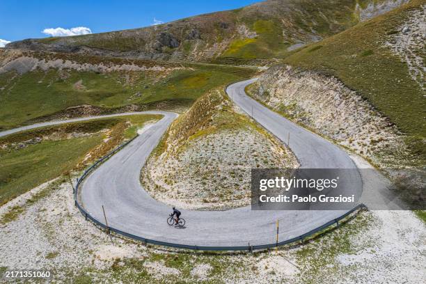 cyclist riding hairpin bend in the mountain - wielrennen stockfoto's en -beelden
