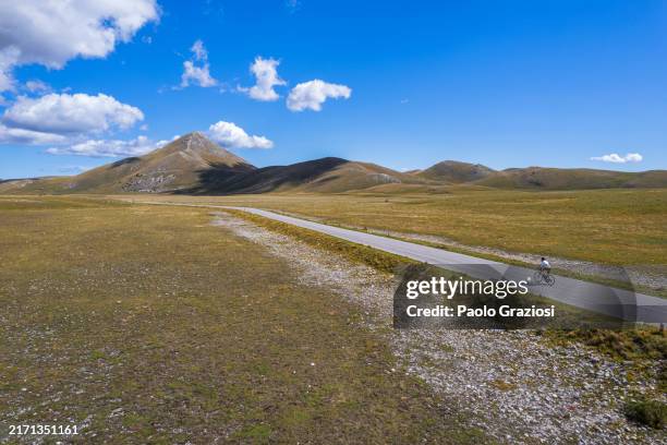 lone cyclist riding a country road - ver stockfoto's en -beelden