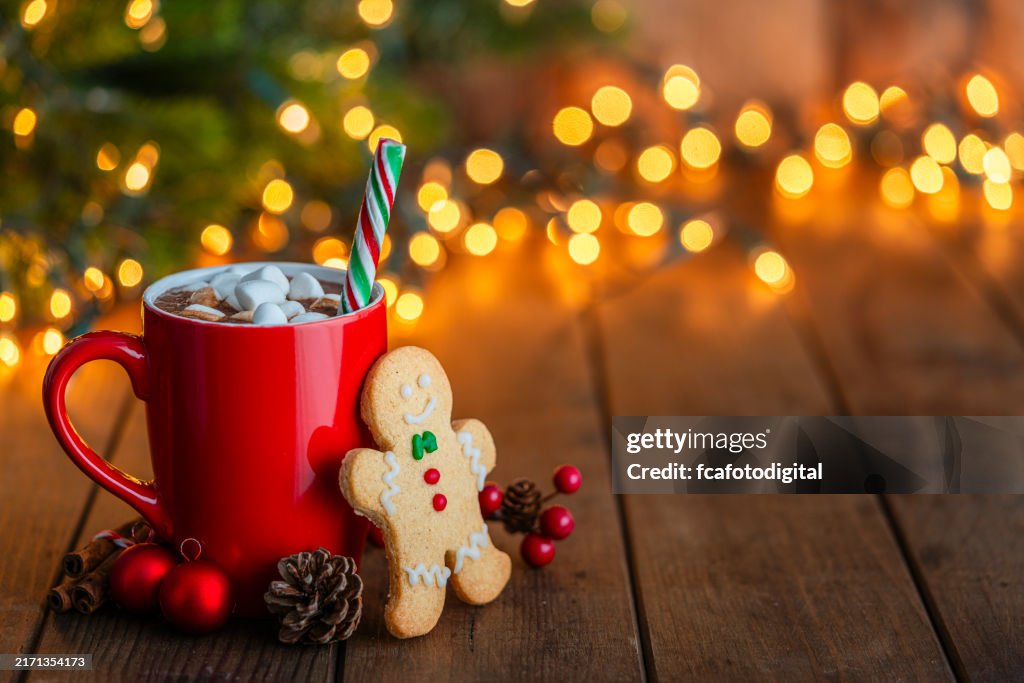 Red mug of hot chocolate with marshmallows and gingerbread man cookie on Christmas table