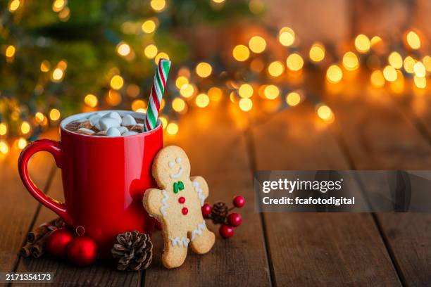 red mug of hot chocolate with marshmallows and gingerbread man cookie on christmas table - hot chocolate stock pictures, royalty-free photos & images