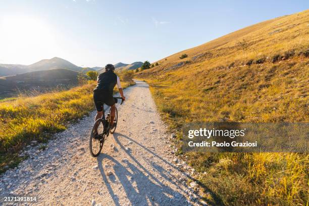 man riding bicycle on a gravel road at sunset - trilho para bicicleta desporto ao ar livre imagens e fotografias de stock