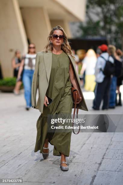 Guest wears dark brown sunglasses, silver earrings, dark green oversized blazer jacket, dark green flowy maxi dress, silver necklace, dark brown...