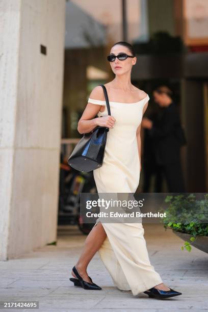 Sophia Roe wears black sunglasses, white off the shoulder maxi dress, shiny black leather bag, outside Toteme, during the New York Fashion week...