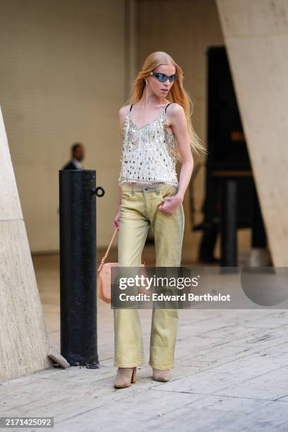 Model wears black sunglasses, silver earrings. White silver metallic sequins top, light green denim jean pants, light brown leather bag, light brown...