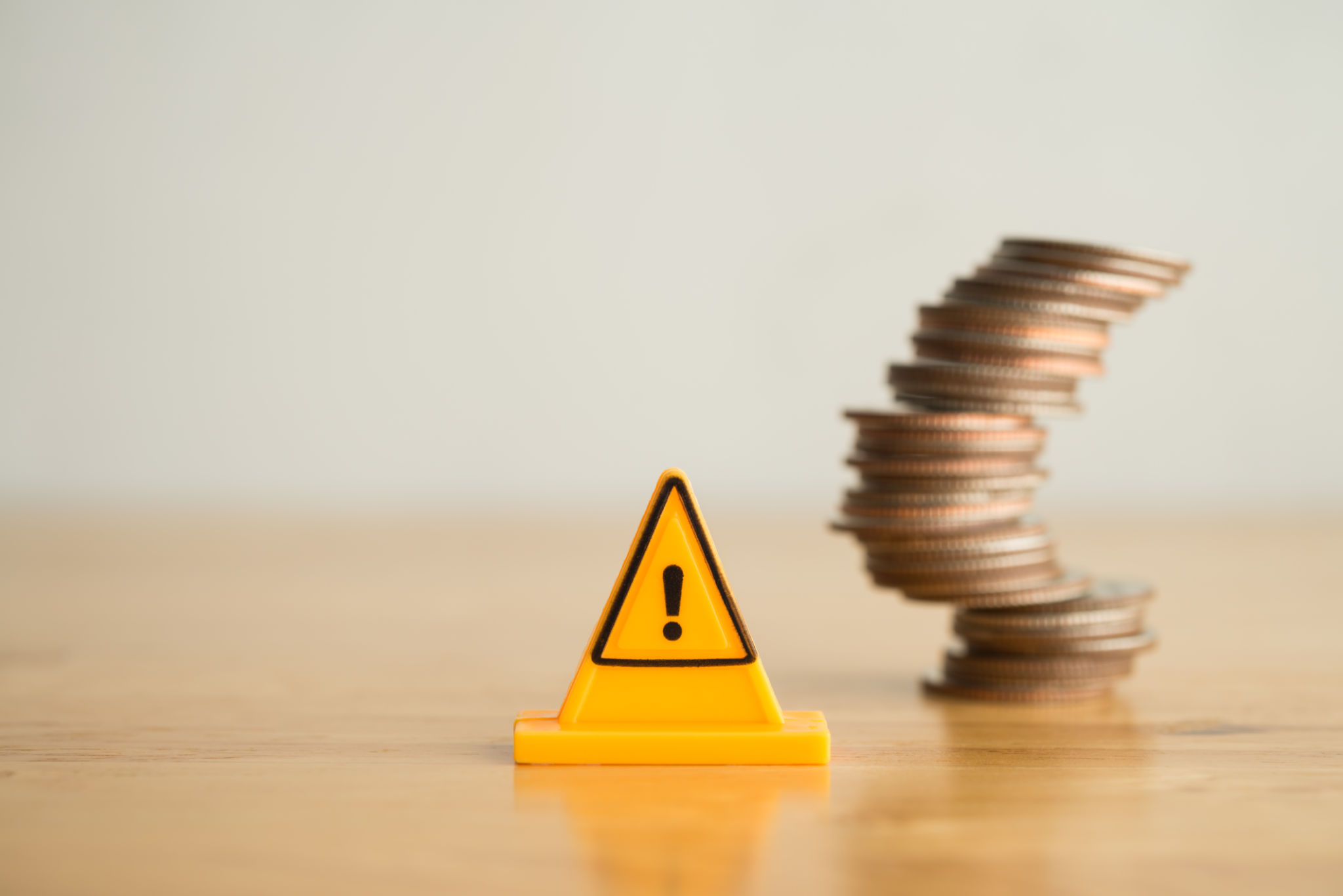 Warning sign label with stack coins in uncertainty situation on wooden table with white background copy space. Warning sign label with stack coins in uncertainty situation on wooden table with white background copy space.