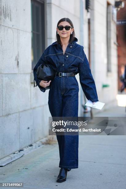 Guest wears black sunglasses, silver earrings, dark navy blue denim jean buttoned up long sleeve romper, black leather belt, shiny black clutch...