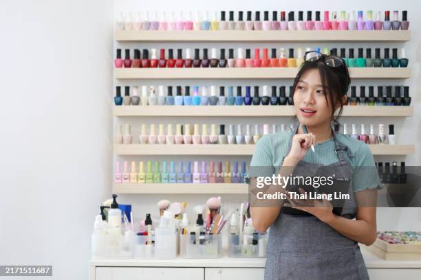 a portrait of a cheerful and confident young asian female small business owner holding a digital tablet while standing in her nail salon store. - nail salon stock pictures, royalty-free photos & images