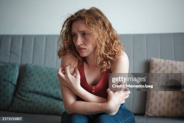 anxiety and itching. nervous stressed woman itching her skin, sitting on sofa at home, feeling anxious. stress rash - neuropathy stock pictures, royalty-free photos & images