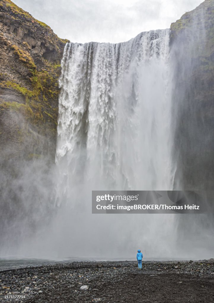A child stands alone in front of Skogafoss waterfall in Iceland