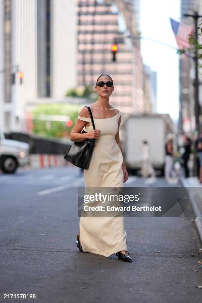 Sophia Roe wears black sunglasses, white off the shoulder maxi dress, shiny black leather bag, outside Toteme, during the New York Fashion week...