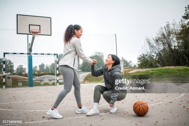 helfende hand nach basketball-sturz mit hispanischen und asiatischen freunden - fairness stock-fotos und bilder