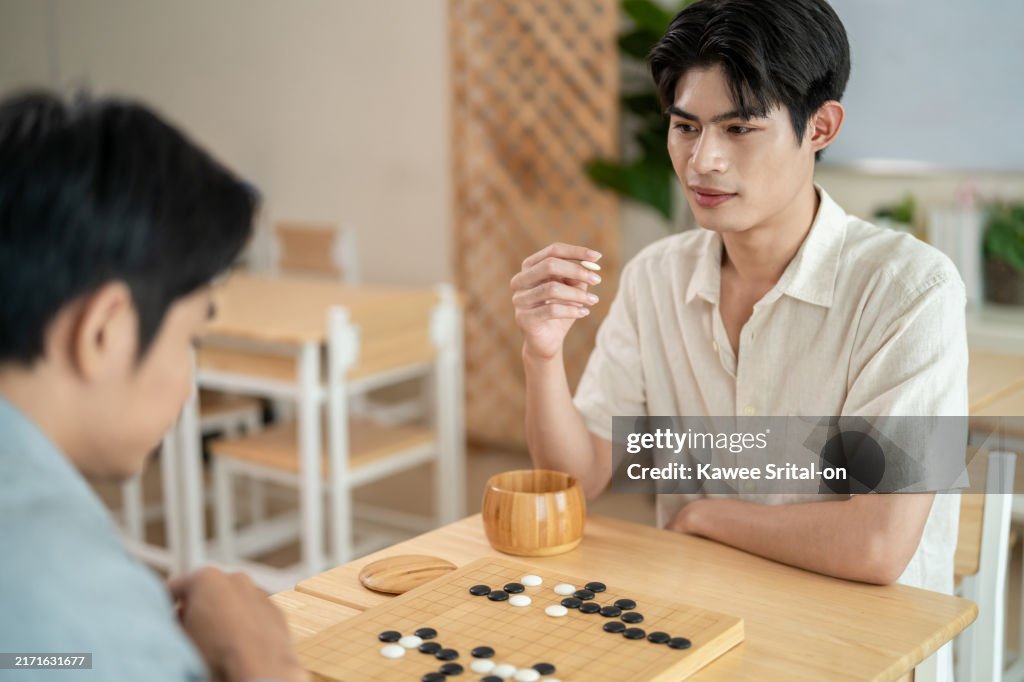 Asian young men playing board game Go during competition in community. Attractive two male friend players participate in traditional asian chinese board game match on a table in the club house center.