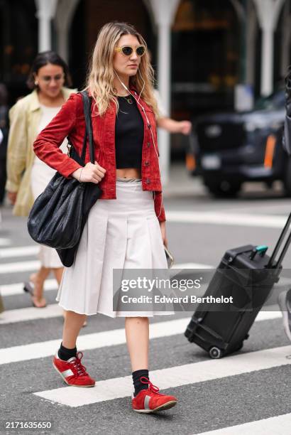 Guest wears light yellow sunglasses, black cropped shirt, dark red suede jacket, shiny black leather bag, cream pleated low-rise midi skirt, black...