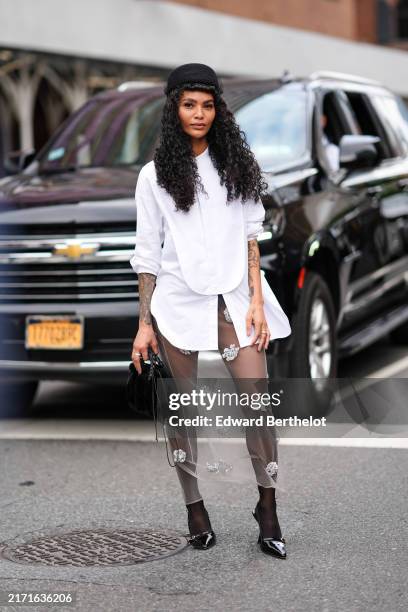 Guest wears black pillbox hat, white button up long sleeve shirt, white sheer mesh tulle floral detail midi skirt, black leather bag, black sheer...