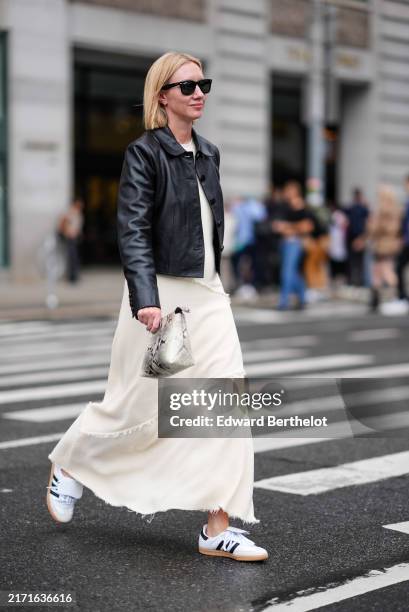 Lisa Aiken wears black sunglasses, shiny black cropped leather jacket, white layered midi dress, light gray white black pattern/print handbag, white...