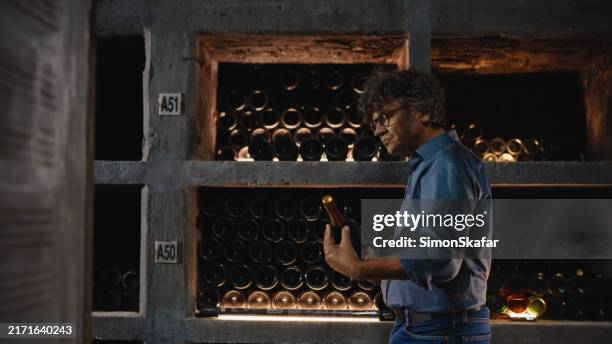 senior winemaker evaluating bottled selection in cellar - wijnkelder stockfoto's en -beelden
