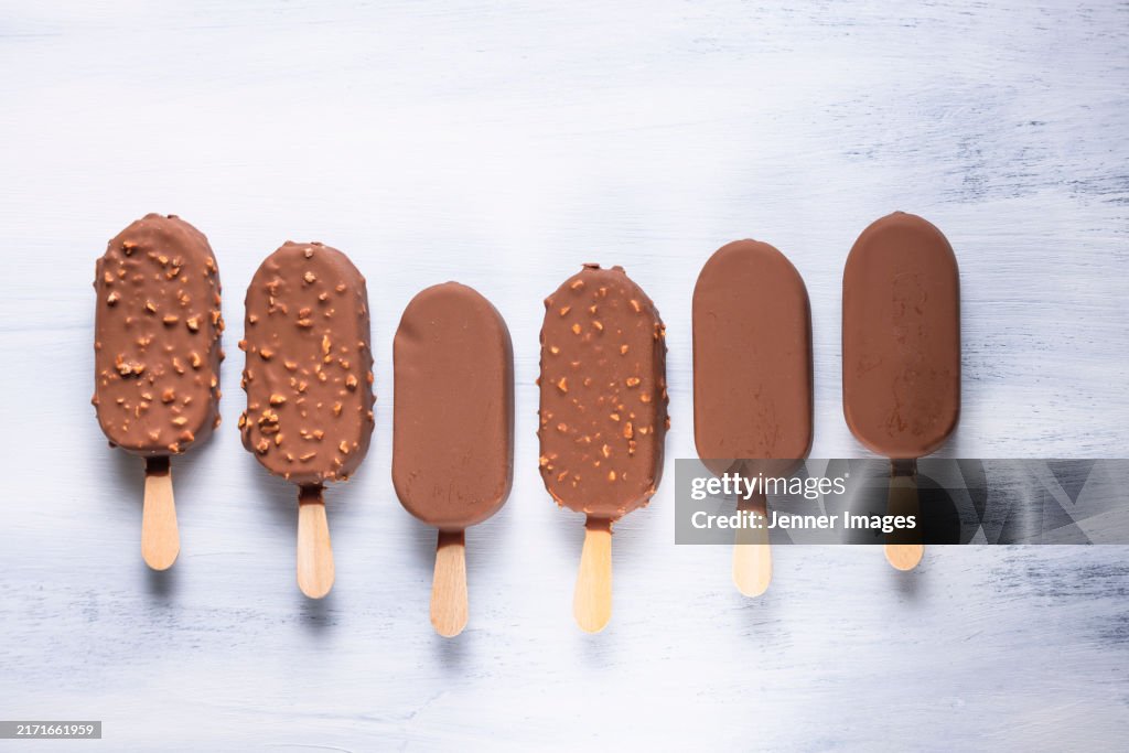 A row of assorted Chocolate popsicle ice cream bars on light coloured background.
