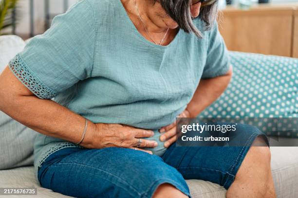 seniorin mit bauchschmerzen auf dem sofa zu hause - diarrhö stock-fotos und bilder