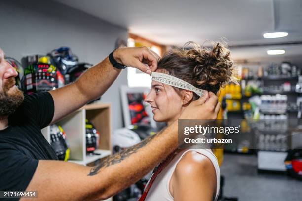 male worker measuring female customer's head for a motorcycle helmet in a moto shop - mid adult stock pictures, royalty-free photos & images
