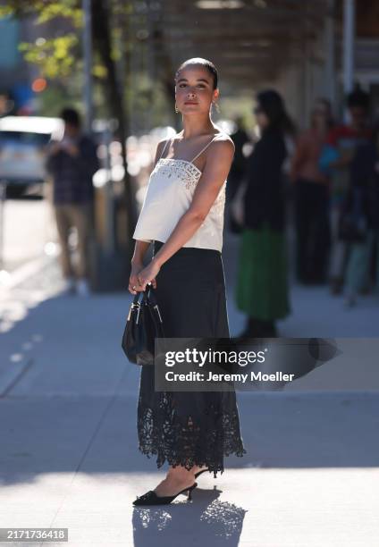 Juliana Canfield is seen wearing gold oval earrings, a cream-white boxy top with lace detail and spaghetti straps from Ulla Johnson, a black...