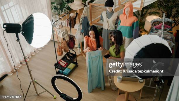 deux jeunes femmes asiatiques présentent un vêtement à un public lors d’une vente en direct pour leur boutique en ligne. - industrie de la mode photos et images de collection