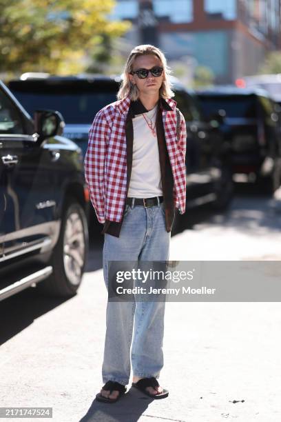 Henrik Morten Lischke is seen wearing several small hoop earrings, squared black sunglasses, a red and white checked jacket over a brown shirt and a...