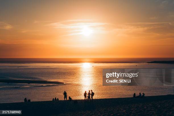 silhouettes of people standing on the beach at the seaside at sunset - arcachon stock pictures, royalty-free photos & images