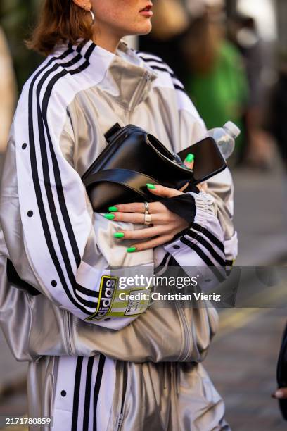 Guest wears silver Adidas track suit, black bag outside Bora Aksu during London Fashion Week September 2024 on September 13, 2024 in London, England.