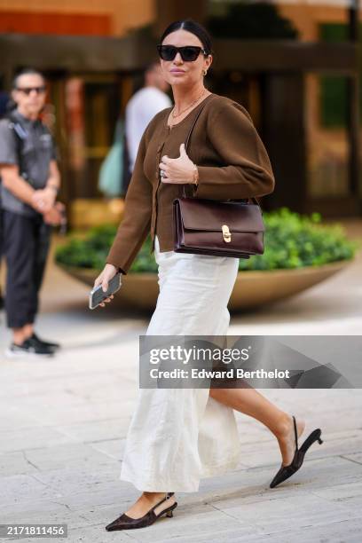 Guest wears sunglasses, earrings, a brown cardigan, a white skirt , pointed shoes, outside Toteme, during New York Fashion Week, on September 10,...