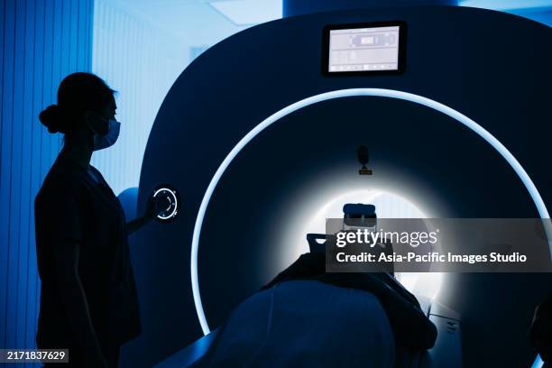 silhouette d’un patient allongé à l’intérieur d’un scanner médical à l’hôpital, l’infirmière fait fonctionner la machine. - scanner à résonance magnétique photos et images de collection