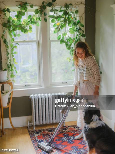 frau staubsaugt mit hund, der neben ihr steht - aufgeräumter raum stock-fotos und bilder