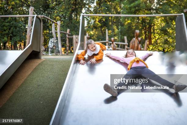 girl with down syndrome laughing while sliding with her friend, fun and friendship at the playground - children only stock pictures, royalty-free photos & images