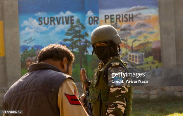 An Indian paramilitary soldier look toward a policeman as he stands guard inside a polling station on September 18, 2024 in Pulwama south of...