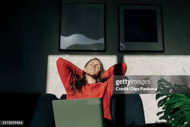 long-haired young man works remotely with a laptop in a sunlit room and takes a break for relaxation - faire-une-pause photos et images de collection