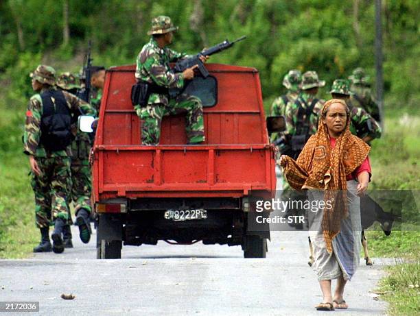 An Acehnese woman walks as members of Indonesian military patrol the main road of Seuneuduee village in Pidie-Aceh, 11 July 2003. Indonesian troops...