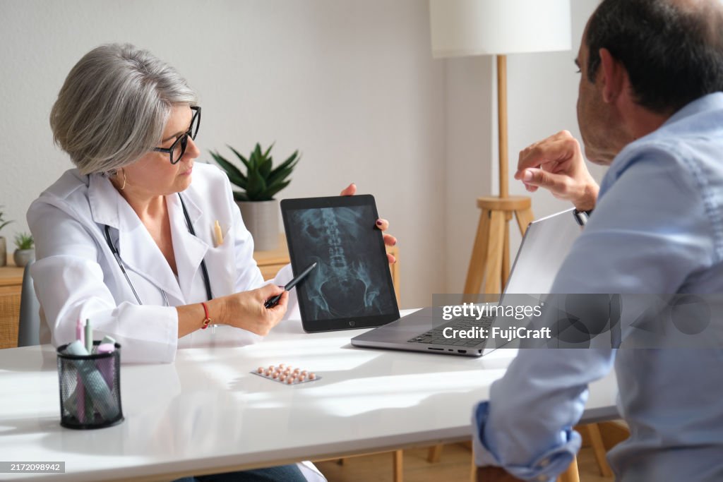 Ärztin zeigt ihrem Patienten Röntgenbild des Beckens auf einem digitalen Tablet in ihrer Praxis