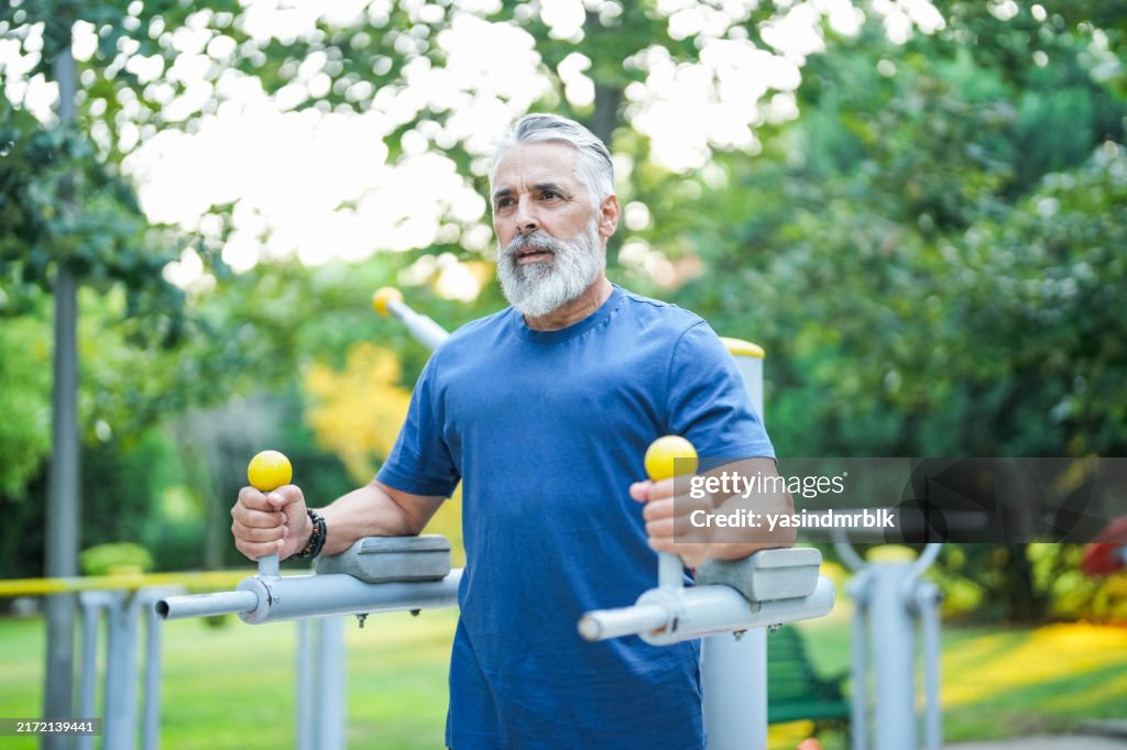 White-haired and bearded man exercising on gym equipment in the park
