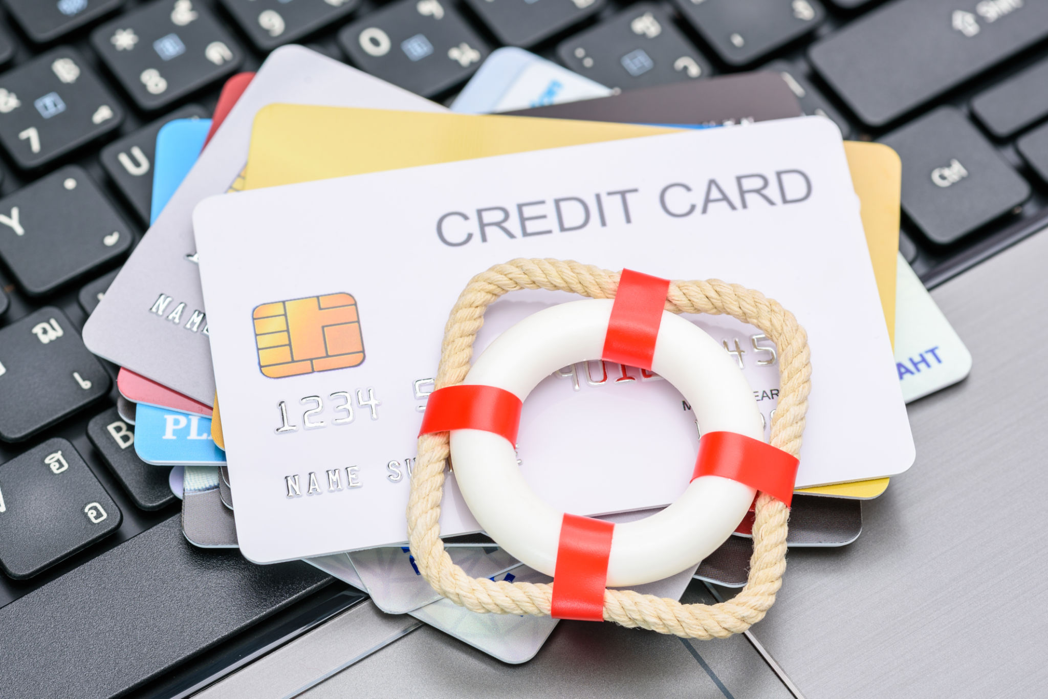Household and credit card debt, personal loan, payment overdue, financial problems : Red lifebuoy or lifebelt atop a stack of credit cards on a laptop, depicting problems in repaying credit card debt. Household and credit card debt, personal loan, payment overdue, financial problems : Red lifebuoy or lifebelt atop a stack of credit cards on a laptop, depicting problems in repaying credit card debt.
