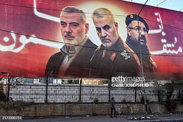 Man walks beneath a giant billboard with the Arabic slogan "we are avenging" behind pictures of the slain figures Palestinian Hamas' political leader...