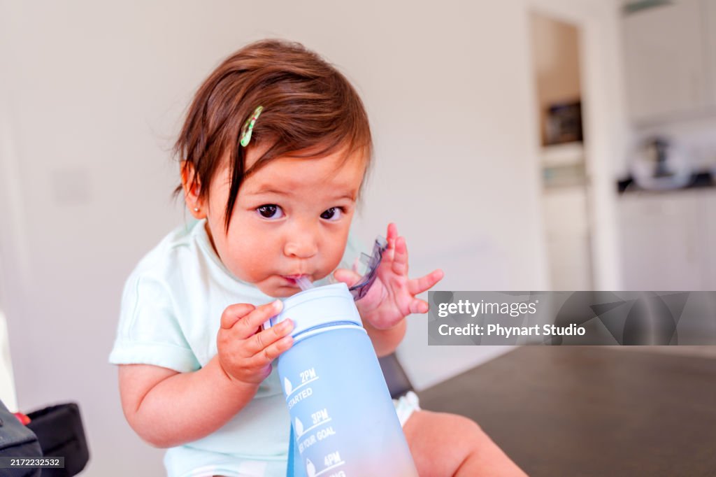 Baby girl drinks water from a water bottle with a straw