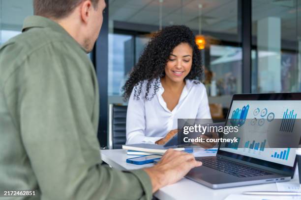 geschäftsmann und geschäftsfrau bei einem treffen im büro. auf dem tisch steht ein laptop mit finanzdiagrammen und grafiken - show stock-fotos und bilder