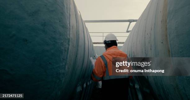 mechanical engineer wearing orange safety jacket and white hardhat with laptop and blueprint working on horizontal water tanks at construction site - engineer stock pictures, royalty-free photos & images