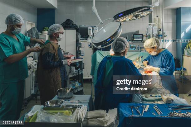 surgical team performing an operation in a hospital operating room with medical equipment and personnel. - operationstisch stock-fotos und bilder
