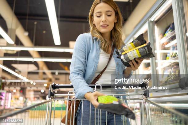 shopping femminile che mette il cibo in un carrello della spesa - cibo precotto foto e immagini stock