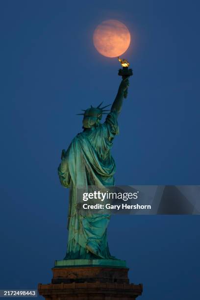 The Harvest Moon illuminated at 98 percent rises behind the Statue of Liberty in New York City one day before turning full on September 16 as seen...