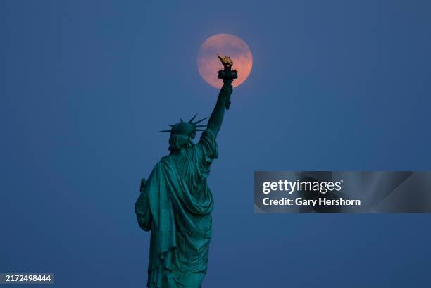 The Harvest Moon illuminated at 98 percent rises behind the Statue of Liberty in New York City one day before turning full on September 16 as seen...